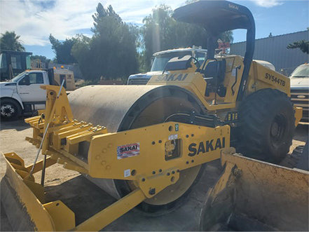 Yellow Sakai roller compactor in an outdoor setting with trees and buildings in the background heavy machinery for sale near Corona CA at Westrax Machinery
